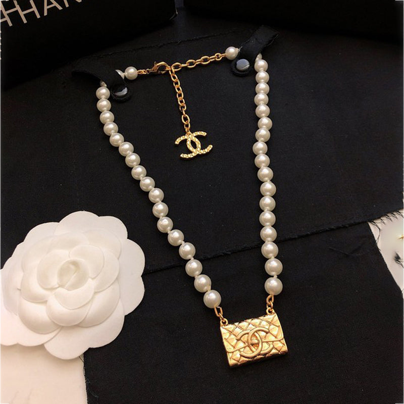 Pearl necklace with gold CC pendant on a black background