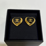 Heart-shaped earrings with gold border and black center logo in a black box.
